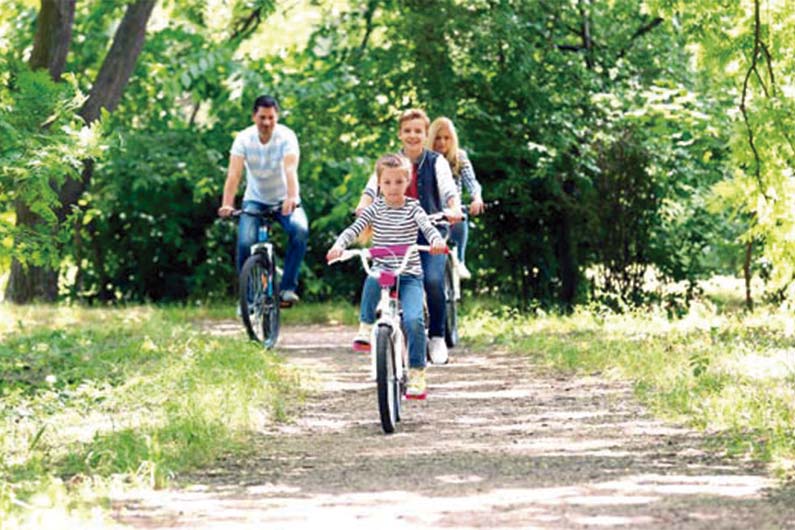 Familia formada por dos adultos y dos niños subidos sobre una bici disfrutando de un recorrido en un parque con árboles