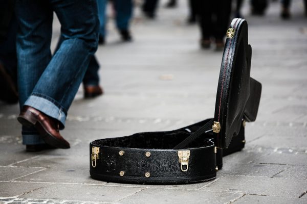 Funda de guitarra apoyada en el suelo en medio de la calle mientras un hombre camina al lado de ella
