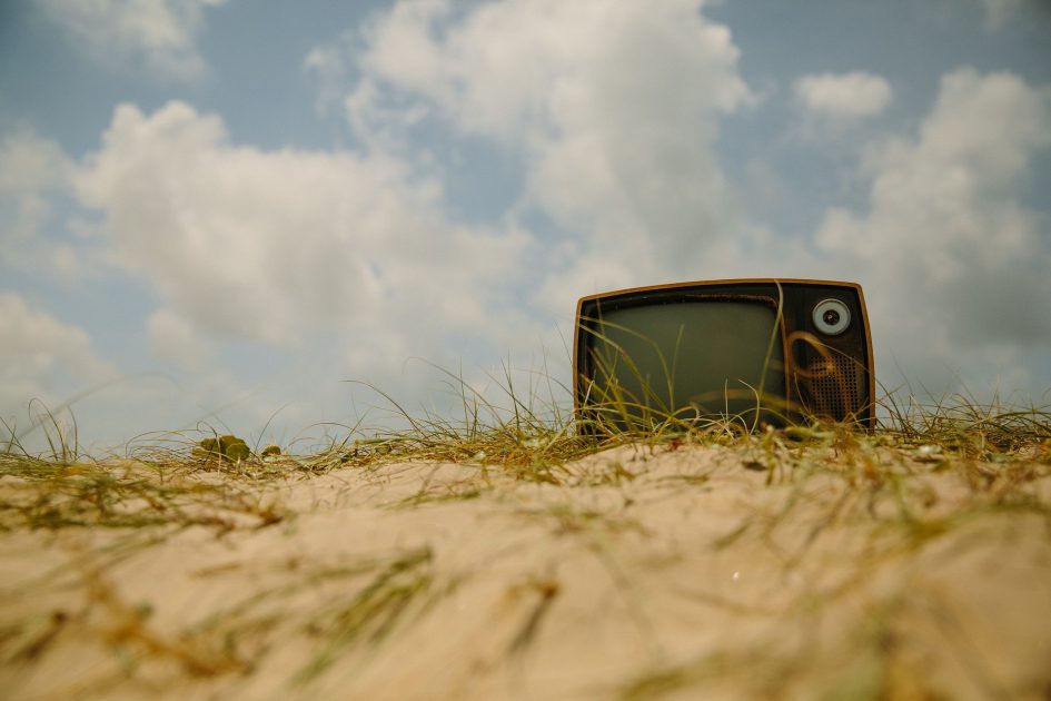 Televisión antigua apoyada sobre suelo arenoso con hierba seca