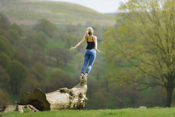 Mujer con los brazos abiertos y respirando aire fresco subida sobre un tronco ubicado en la naturaleza